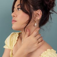 Boucles d'oreilles et bagues en or sur femme Femme avec boucles d'oreilles et bagues en or, haut jaune, fond bleu