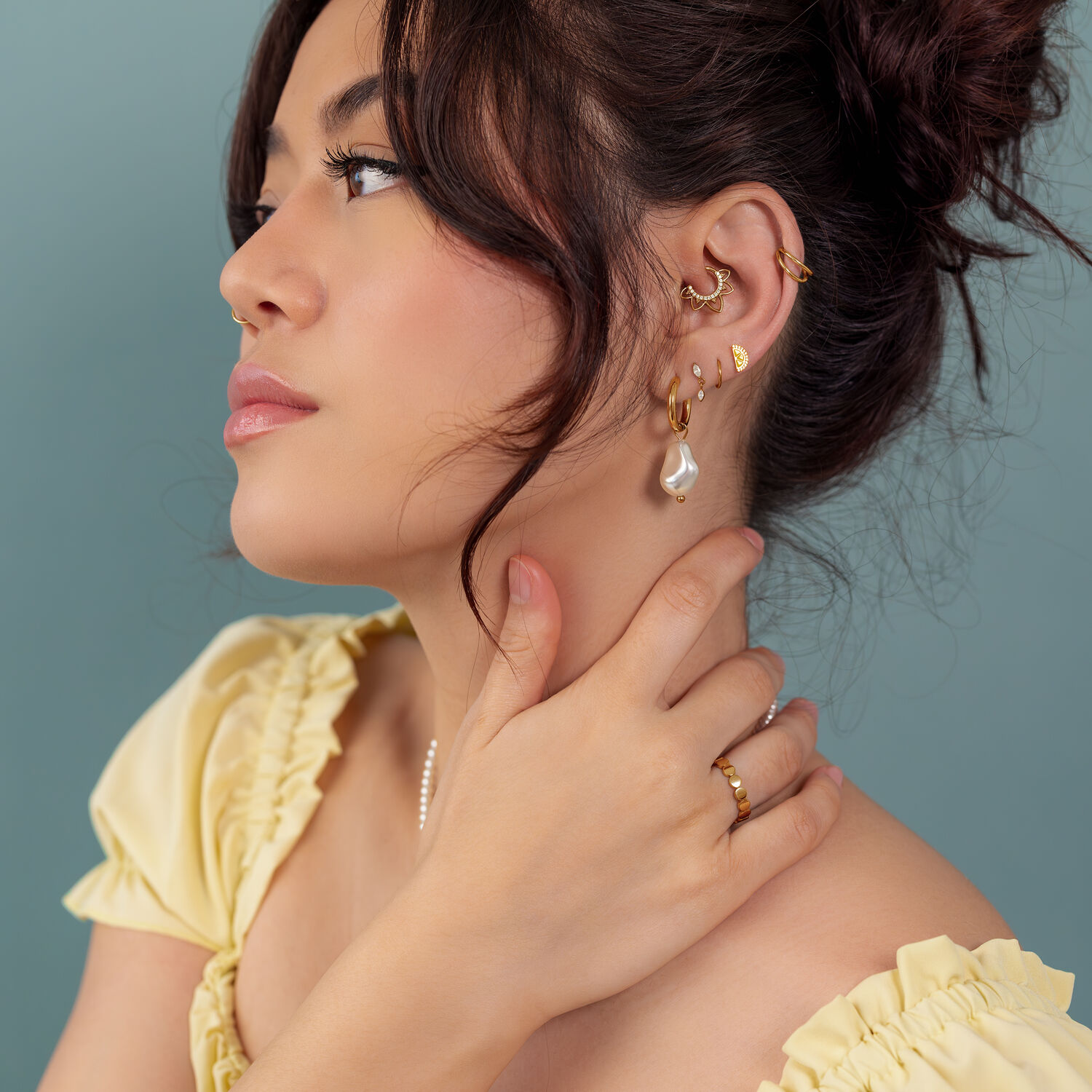 Boucles d'oreilles et bagues en or sur femme Femme avec boucles d'oreilles et bagues en or, haut jaune, fond bleu