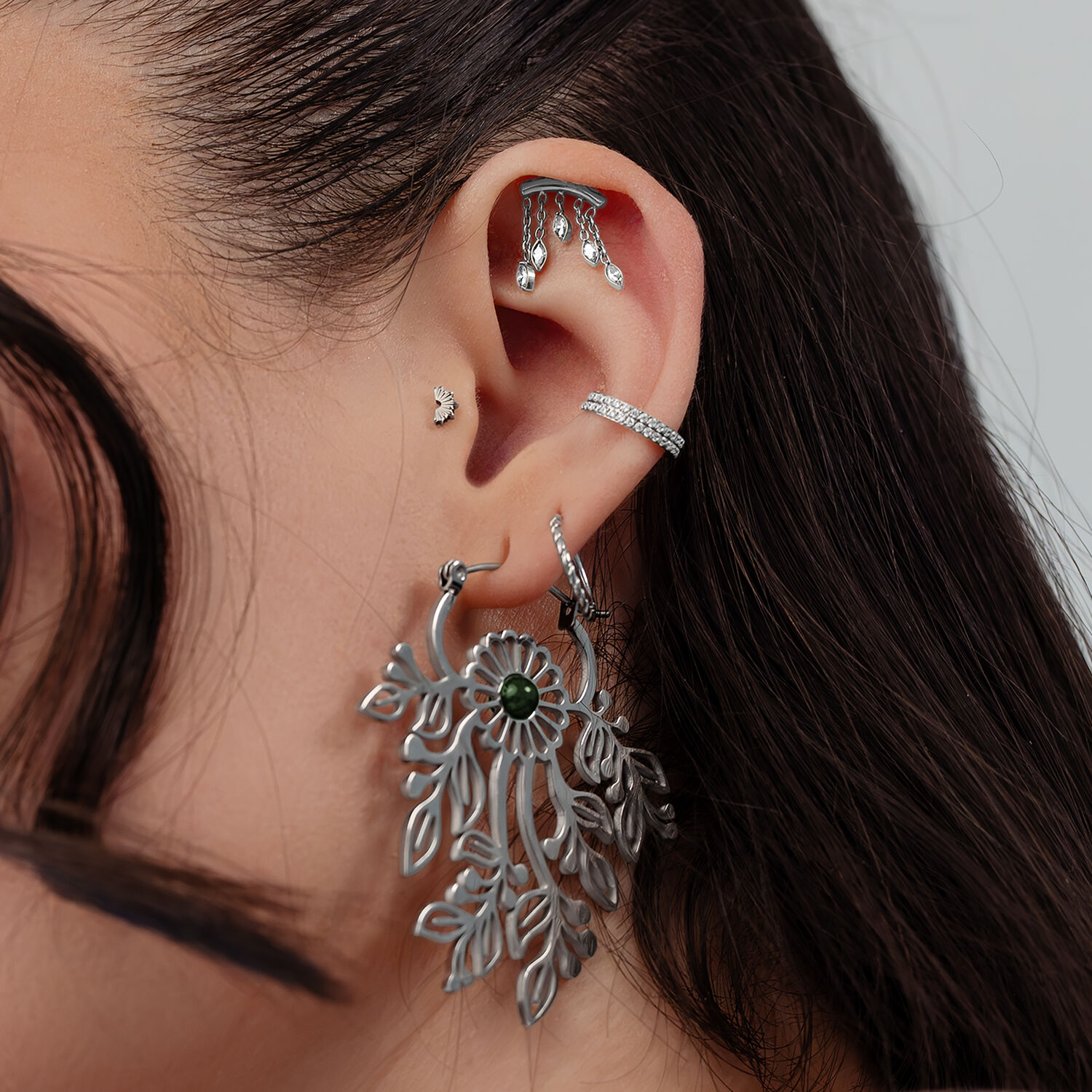 Embouts de piercing d'oreille hélice argentés Gros plan d'une oreille avec plusieurs piercings argentés, y compris un grand pendentif ovale et des embouts étincelants.