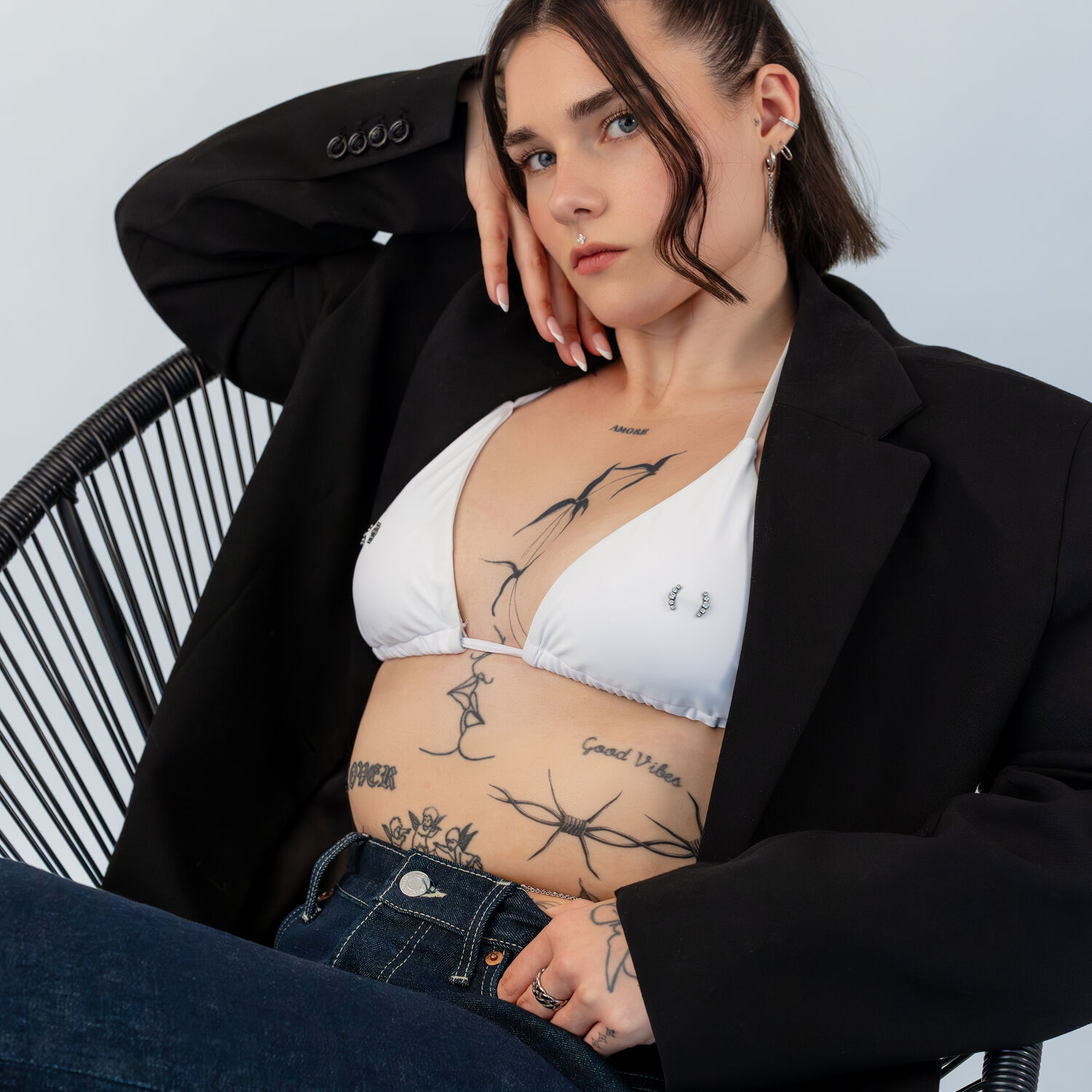 Femme en haut de bikini blanc et blazer noir sur une chaise, avec un torse tatoué