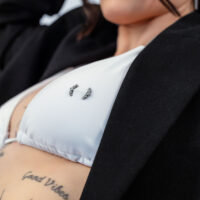 Gros plan d'un haut de bikini blanc avec piercing Penta Crystal Barbell et tatouages en arrière-plan.