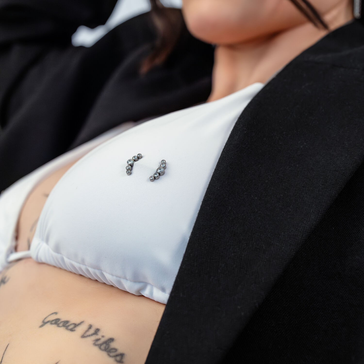 Gros plan d'un haut de bikini blanc avec piercing Penta Crystal Barbell et tatouages en arrière-plan.