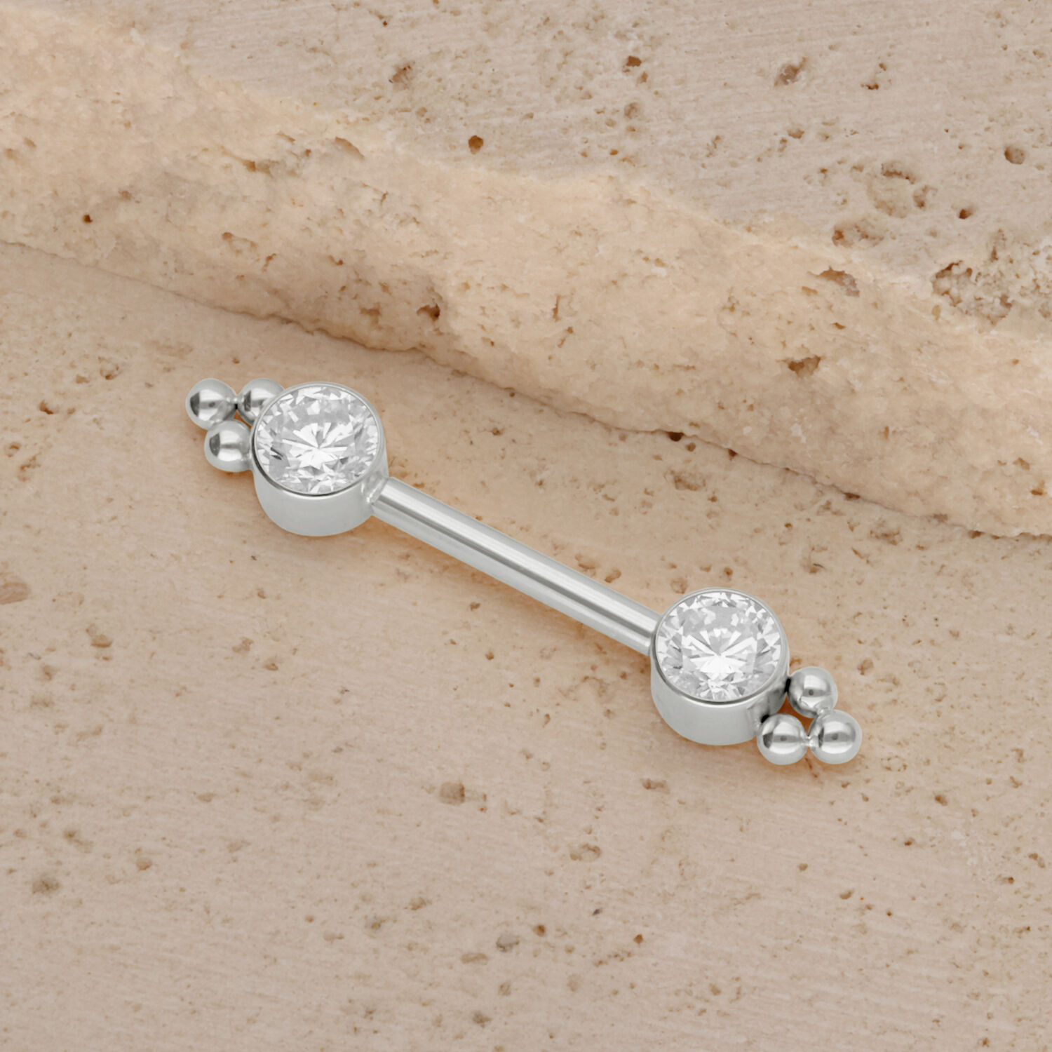 Barbell en or blanc pour téton avec zirconia Barbell en titane blanc avec deux zirconias sur fond sablonneux