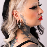 Femme avec boucle d'oreille en forme de V argentée, cheveux noirs, cou tatoué