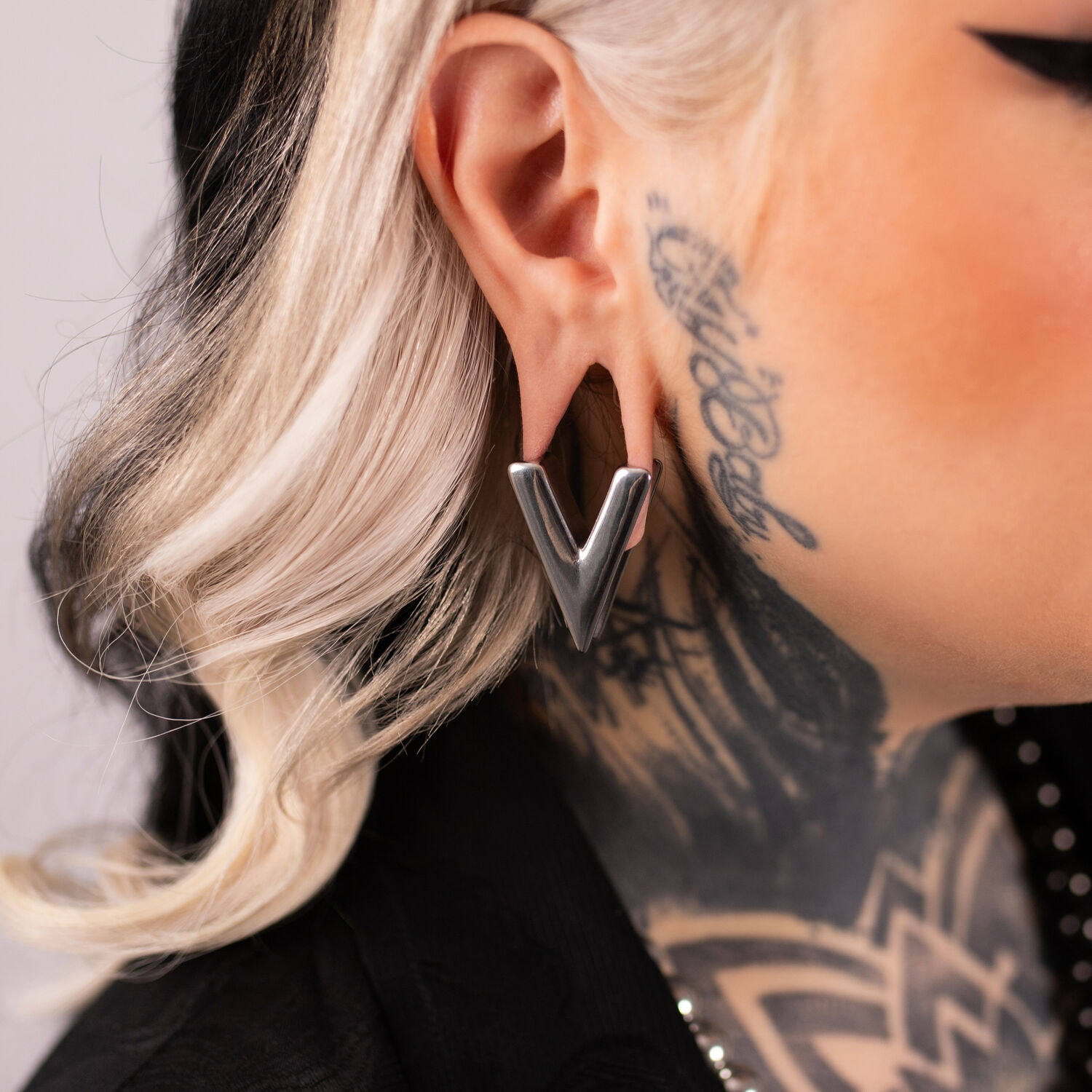 Clou d'oreille en argent en forme de V dans l'oreille d'une personne tatouée, profil latéral