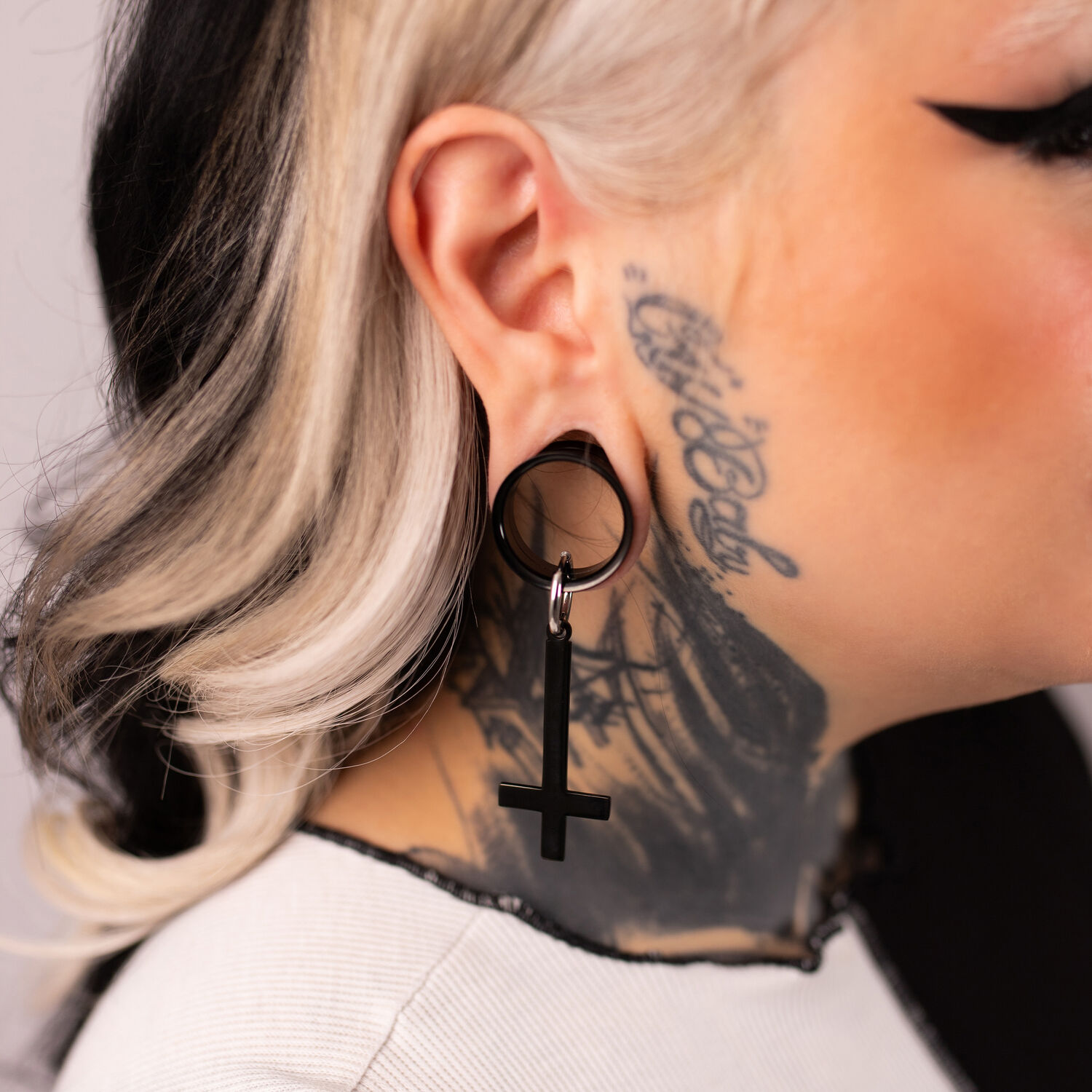 Boucles d'oreilles Cross Hoops noires en acier chirurgical 316L sur une oreille avec tatouage