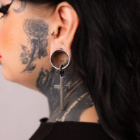 Boucles d'oreilles croisées en argent et noir sur une oreille tatouée