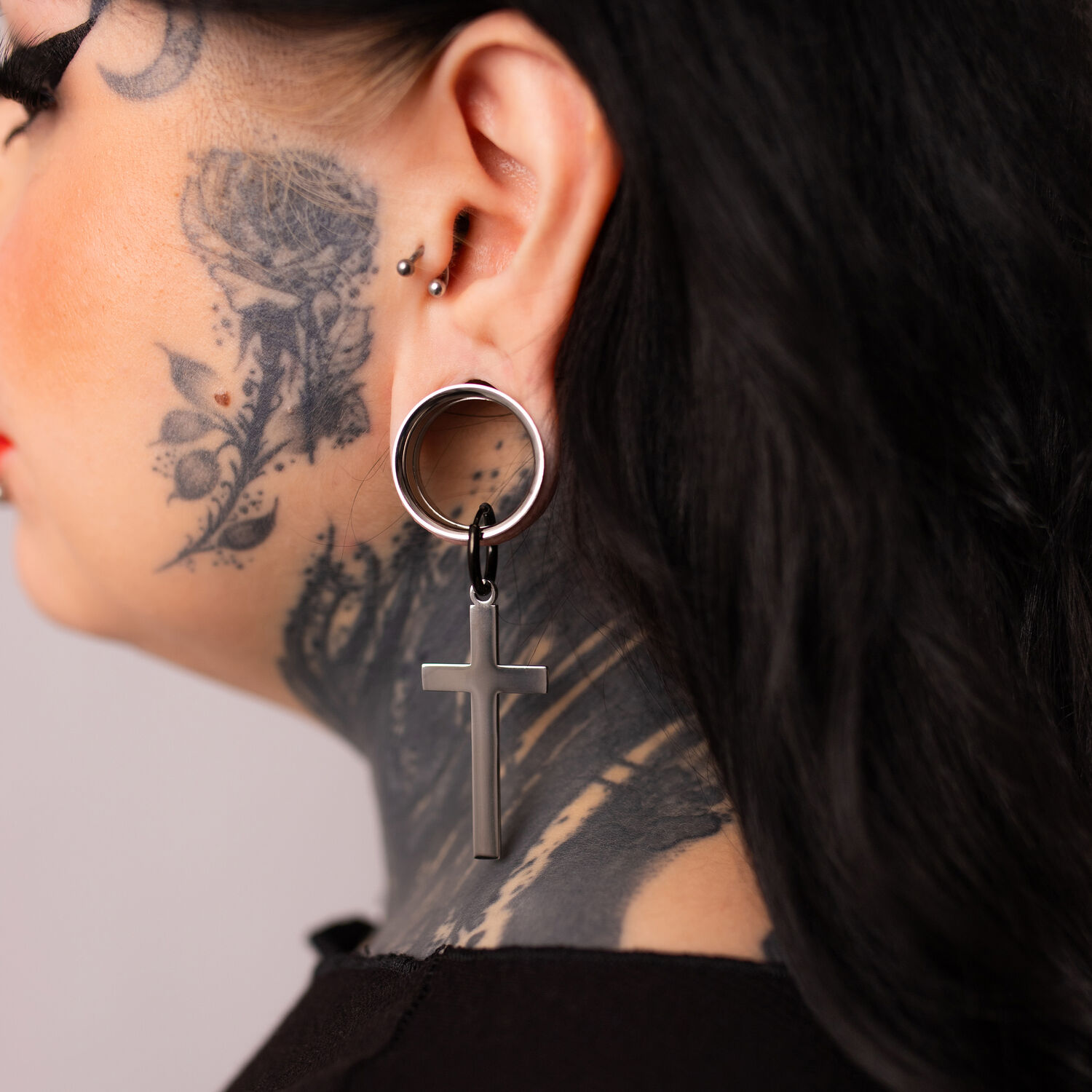Boucles d'oreilles croisées en argent et noir sur une oreille tatouée