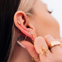 Piercings dorés à l'oreille avec bijoux Gros plan d'une oreille avec plusieurs piercings dorés et bijoux, main tenant l'oreille