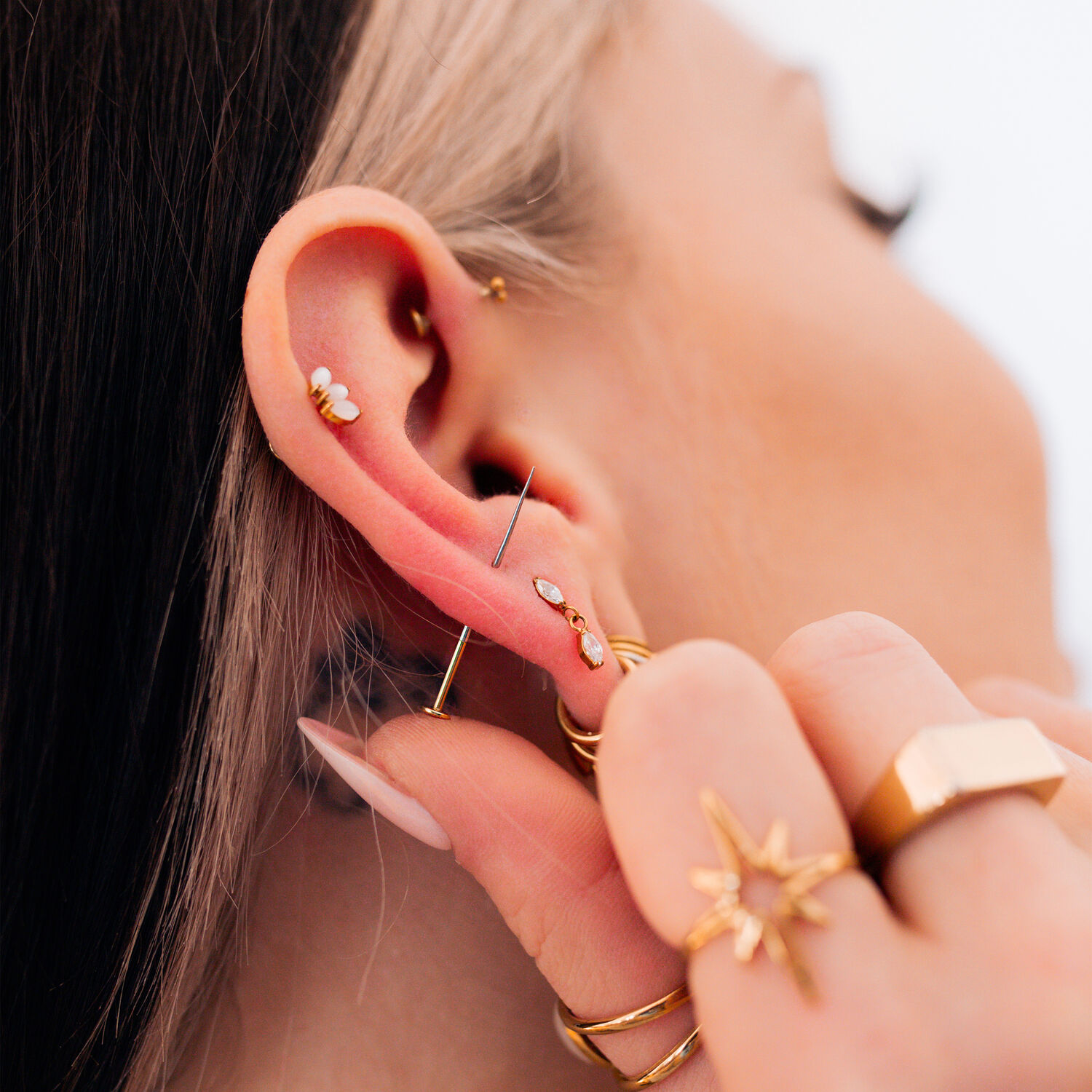 Piercings dorés à l'oreille avec bijoux Gros plan d'une oreille avec plusieurs piercings dorés et bijoux, main tenant l'oreille