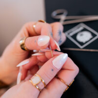 Kit de changement de piercing avec aiguille Mains avec de longs ongles blancs tenant une aiguille de piercing sur fond noir