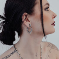 Femme aux cheveux noirs portant des boucles d'oreilles épineuses argentées sur fond clair