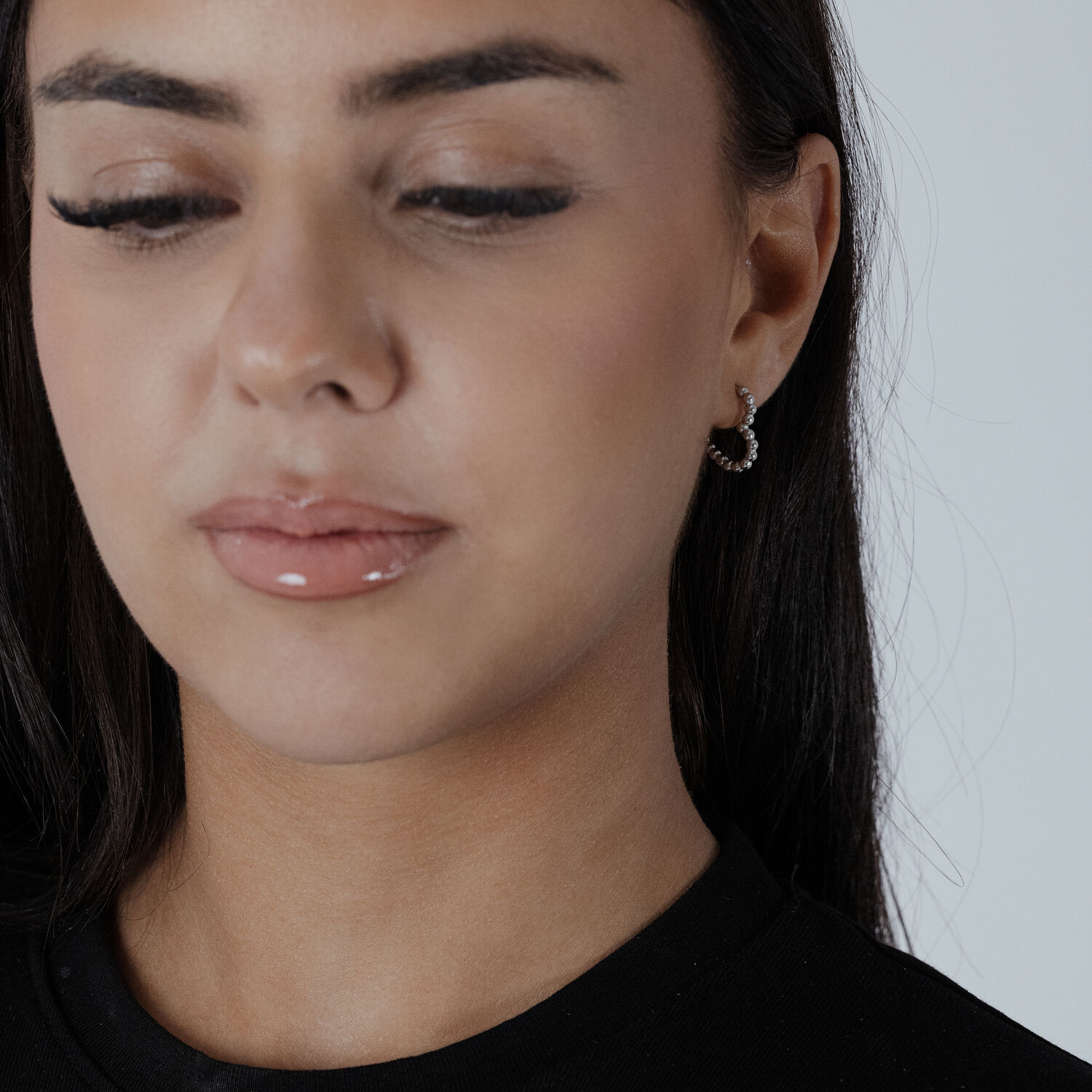 Créoles en forme de cœur en argent Créoles cœur en argent portées à une oreille par une personne en haut noir