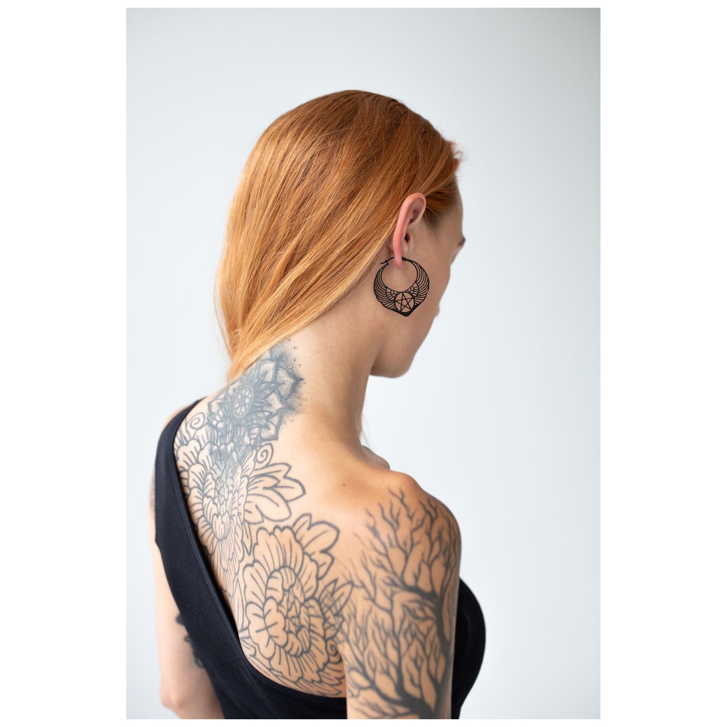 Boucles d'oreilles pentagramme noires à l'oreille Femme aux cheveux rouges portant des boucles d'oreilles pentagramme noires sur fond blanc