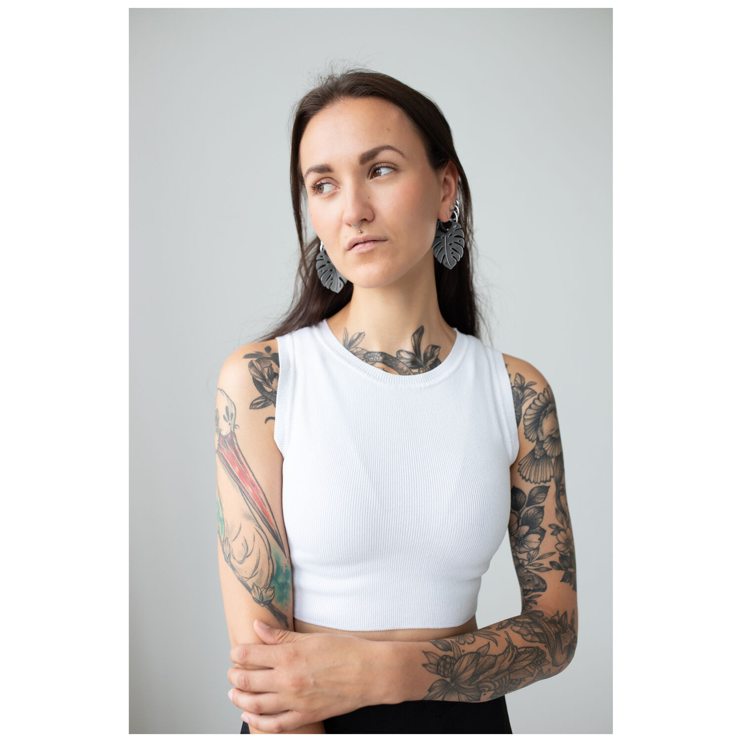 Monstera Leaf Hoops avec femme en studio Femme aux bras tatoués portant des boucles d'oreilles Monstera Leaf Hoops, top blanc