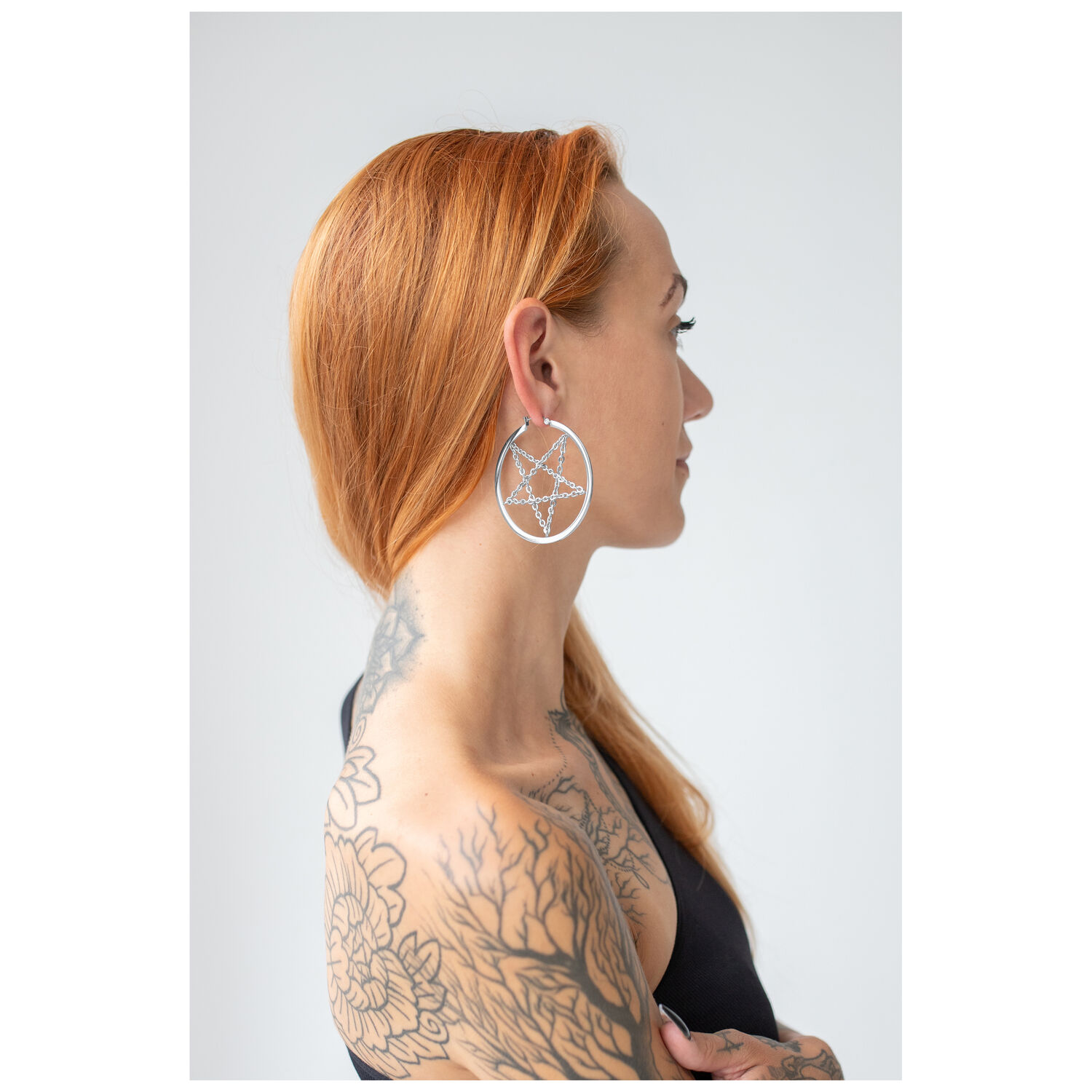 Boucles d'oreilles pentagramme argentées portées par une femme aux cheveux rouges sur fond blanc