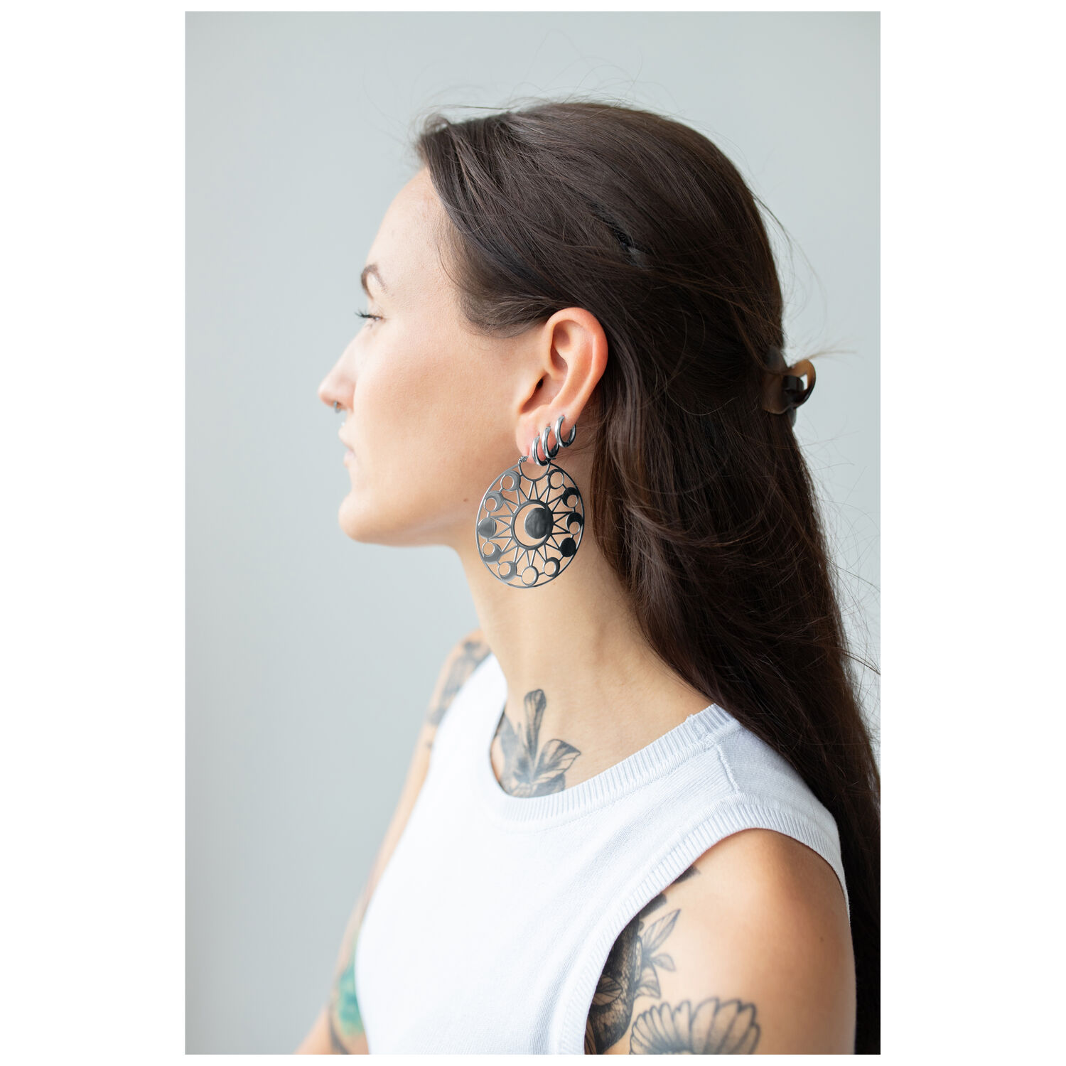 Moon Eclipse Hoops portés par une femme Femme aux longs cheveux noirs portant de grandes boucles d'oreilles rondes avec motif de lune sur fond gris