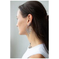 Boucles d'oreilles Oracle Hoops stylées en noir Jeune femme aux longs cheveux portant de grandes boucles d'oreilles Oracle Hoops noires de profil