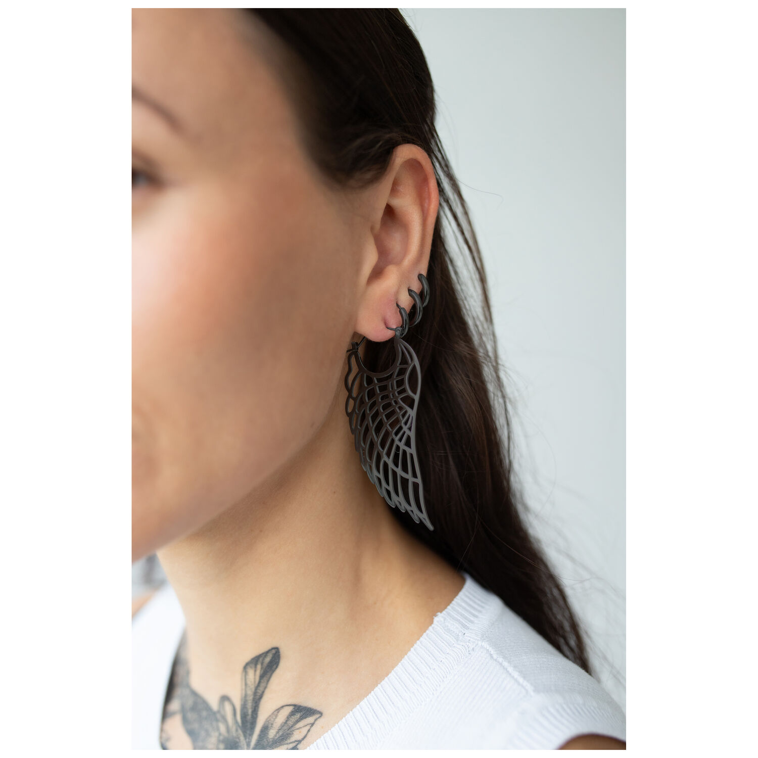 Gros plan sur des boucles d'oreilles Wing Hoops noires portées par une personne aux longs cheveux foncés
