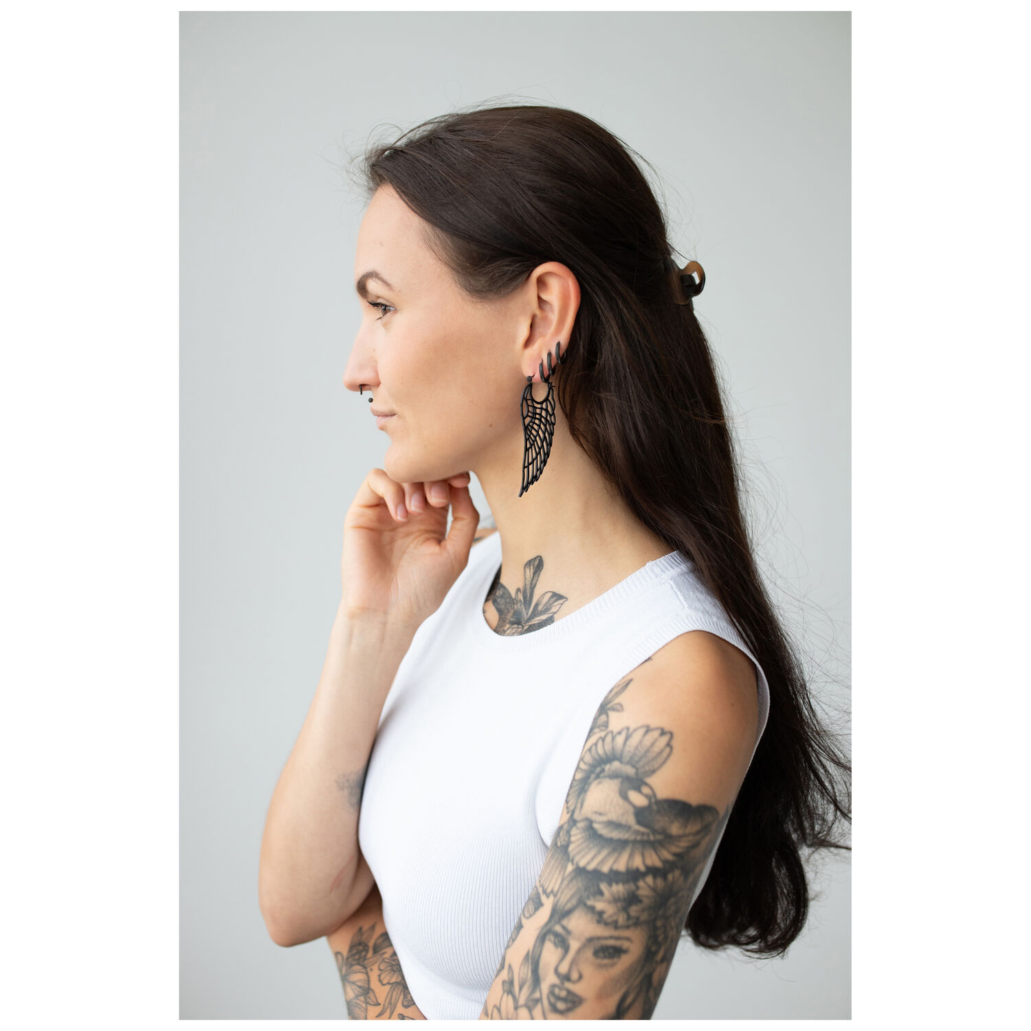 Femme aux longs cheveux noirs, portant des boucles d'oreilles Wing Hoops noires et un haut blanc
