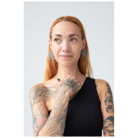 Femme aux cheveux roux portant des boucles d'oreilles Mandala en argent, tatouages visibles