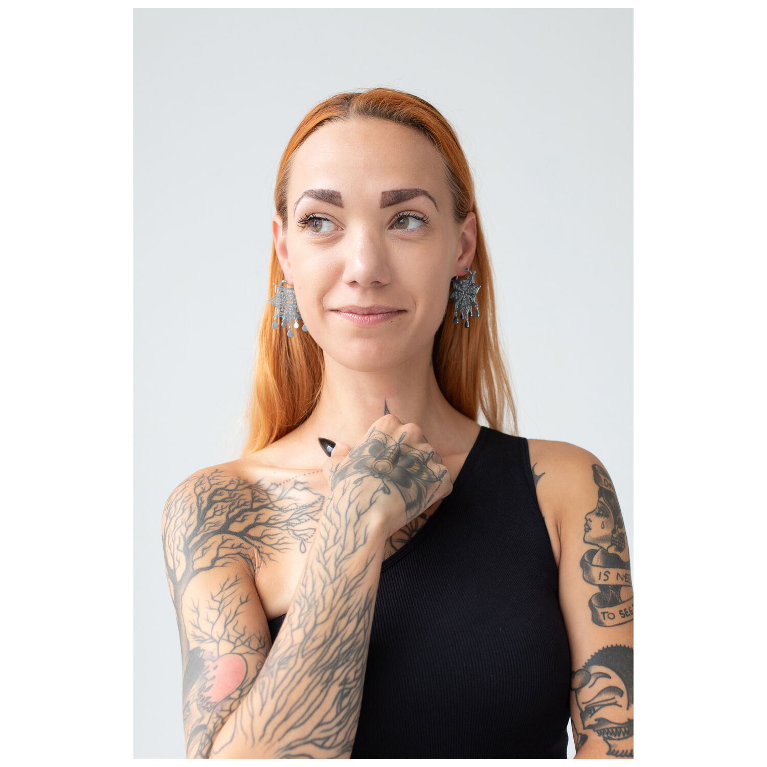 Femme aux cheveux roux portant des boucles d'oreilles Mandala en argent, tatouages visibles