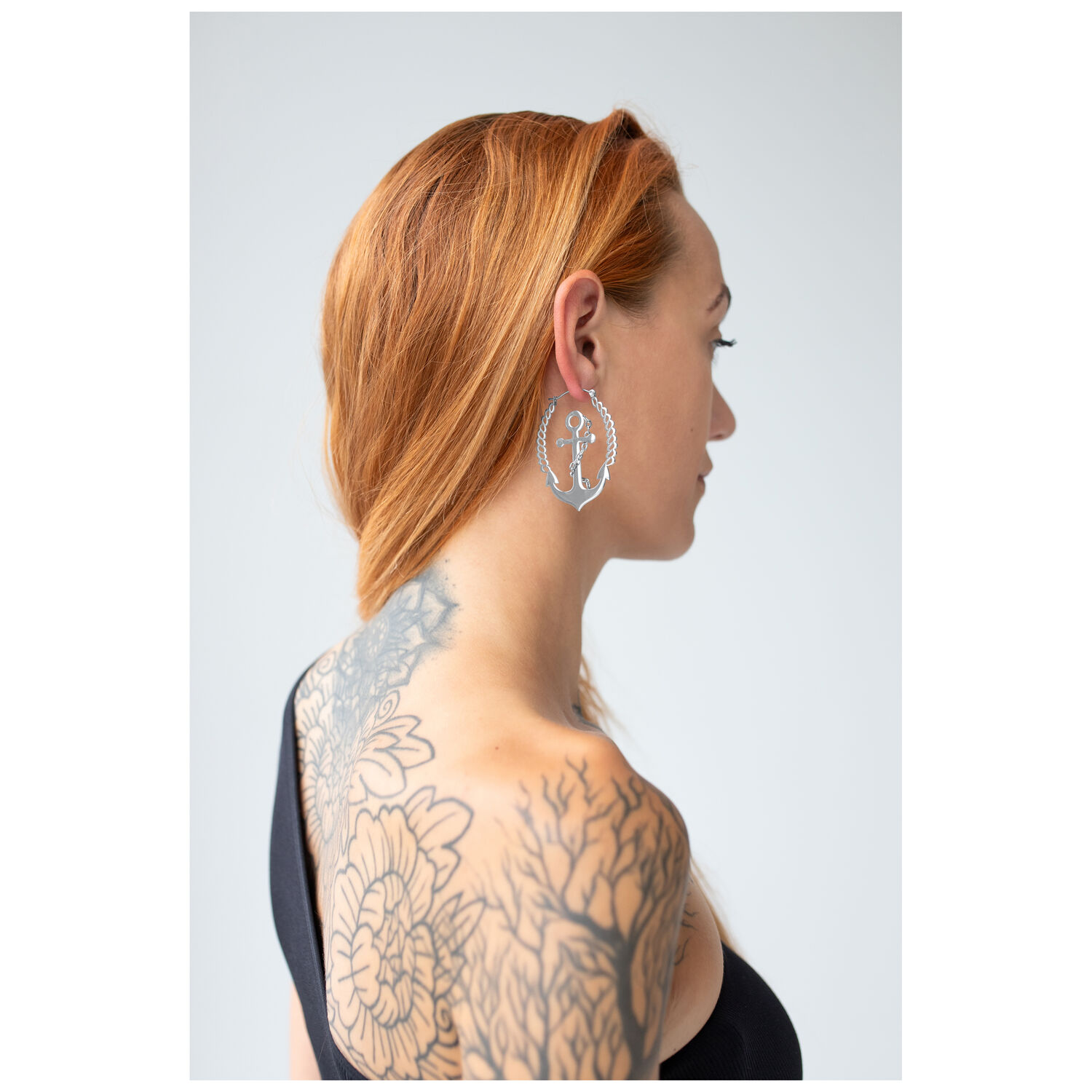 Boucles d'oreilles Chain Anchor Hoops stylées Femme aux cheveux roux portant des boucles d'oreilles Chain Anchor Hoops en argent sur fond clair