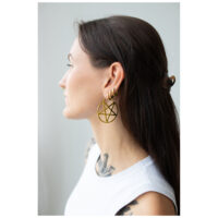 Jeune femme aux longs cheveux foncés portant de grandes boucles d'oreilles pentagramme dorées, photographiée de côté