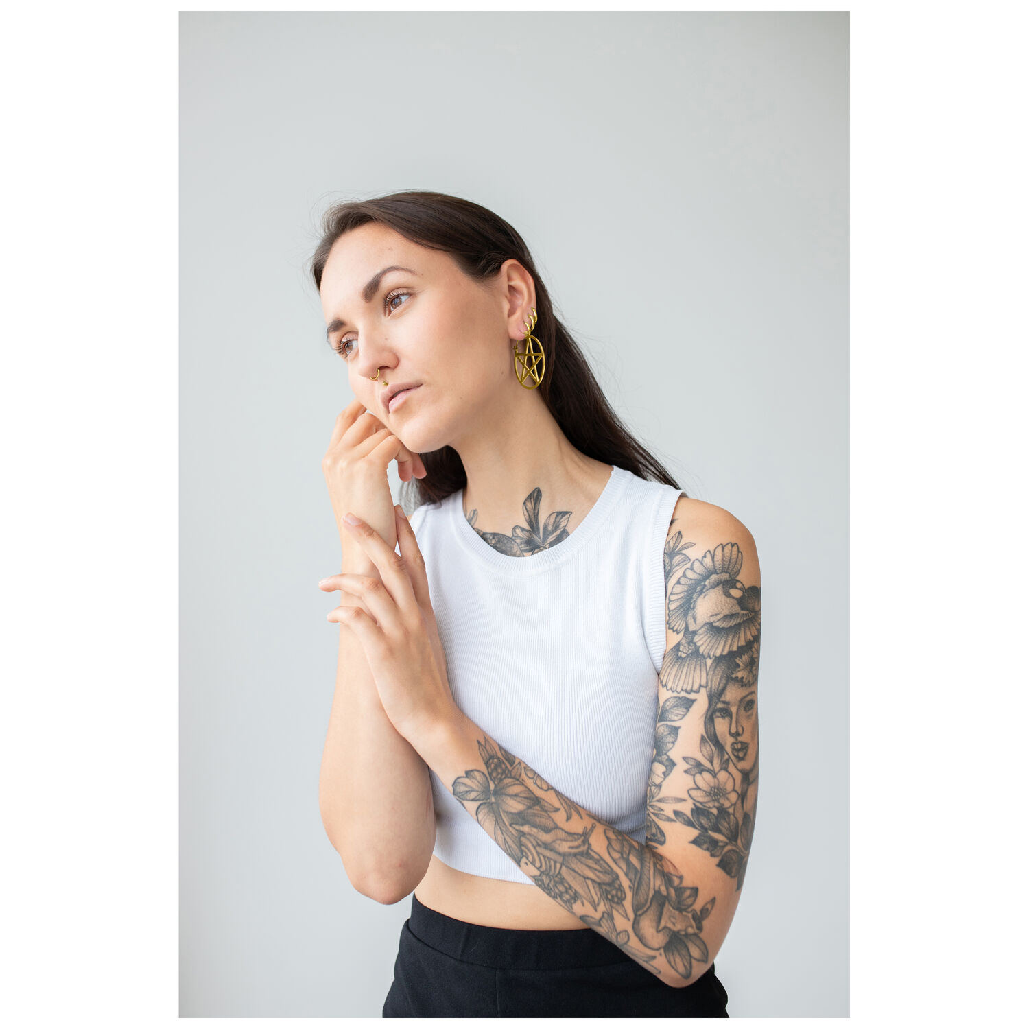 Femme en haut blanc portant des créoles Pentagramme dorées, tatouages visibles