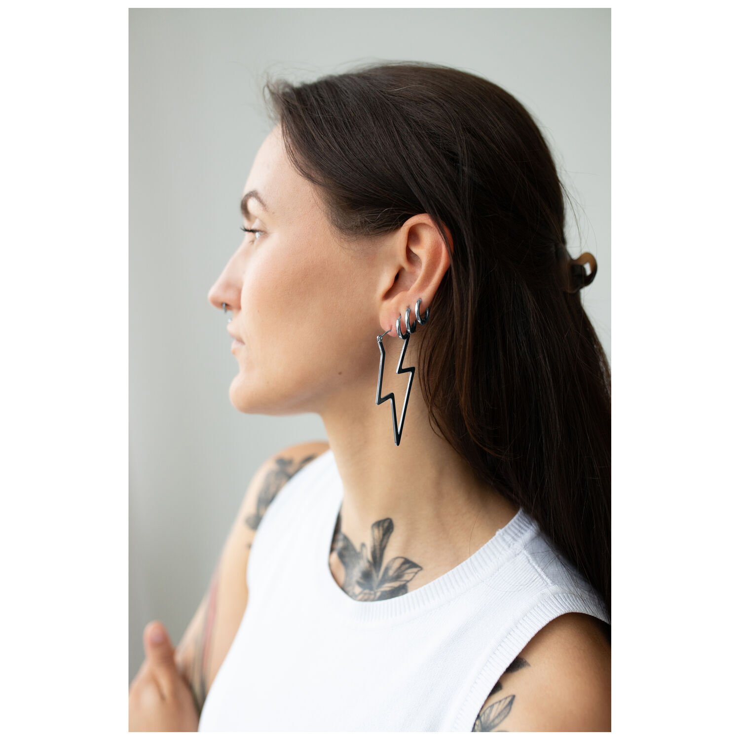 Boucles d'oreilles Thunderbolt Hoops stylées en noir Femme aux cheveux longs portant des boucles d'oreilles éclairs noires en acier, portrait de côté