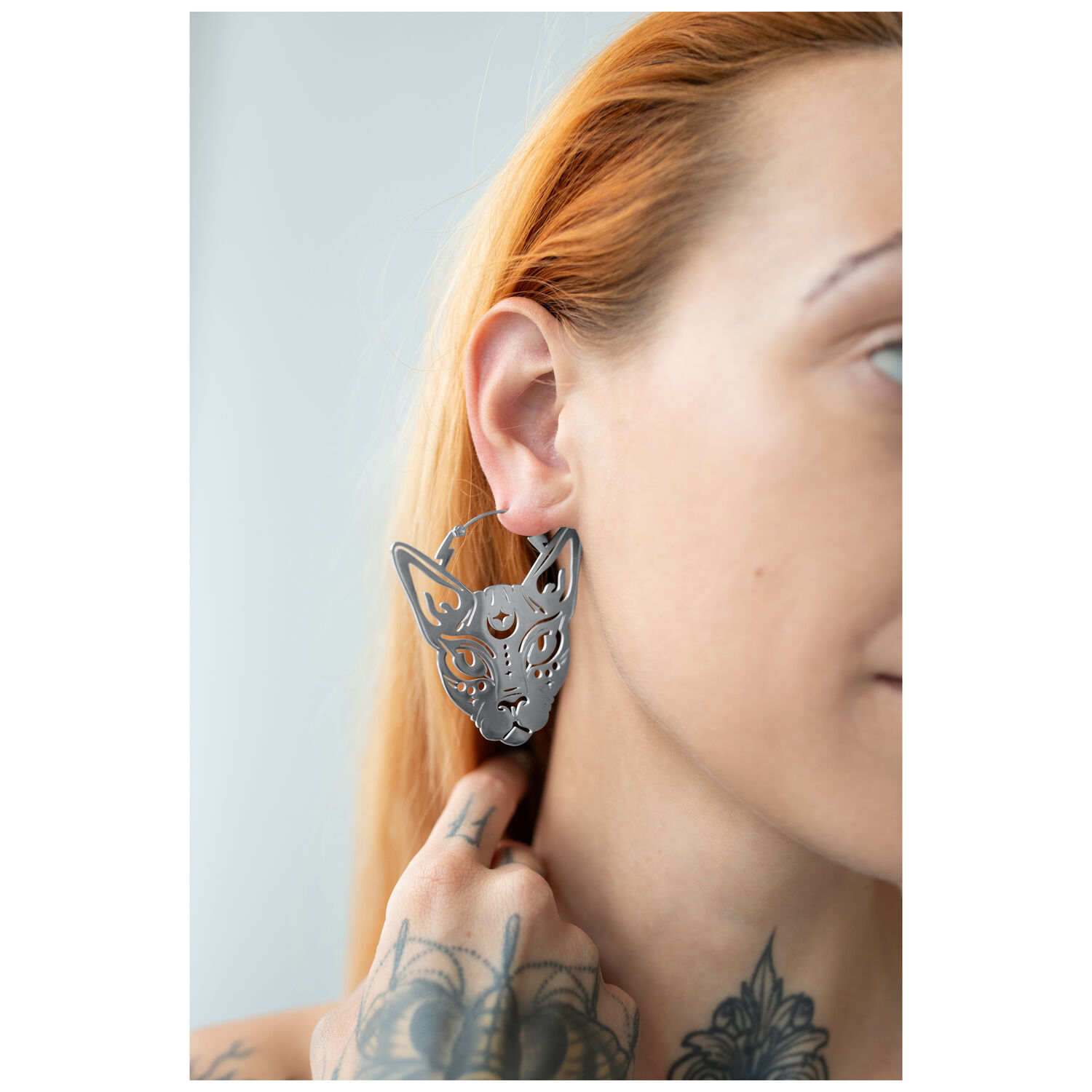 Sphynx Hoops boucles d'oreilles en acier chirurgical Boucles d'oreilles Sphynx Hoops en argent sur une oreille avec une main tatouée