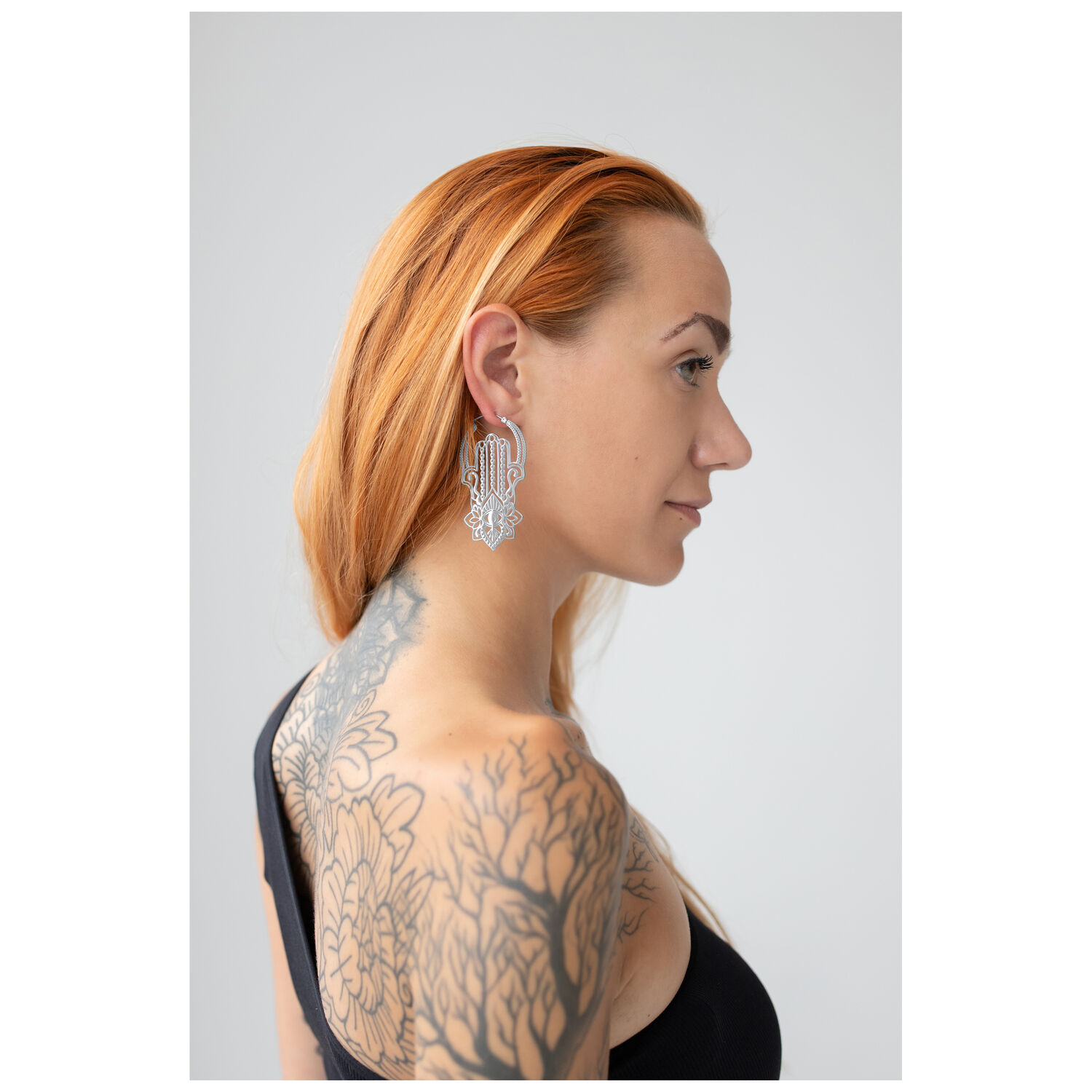 Boucles d'oreilles Khamsa Hoops élégantes en argent Femme aux longs cheveux auburn portant des boucles d'oreilles Khamsa Hoops en argent sur fond neutre
