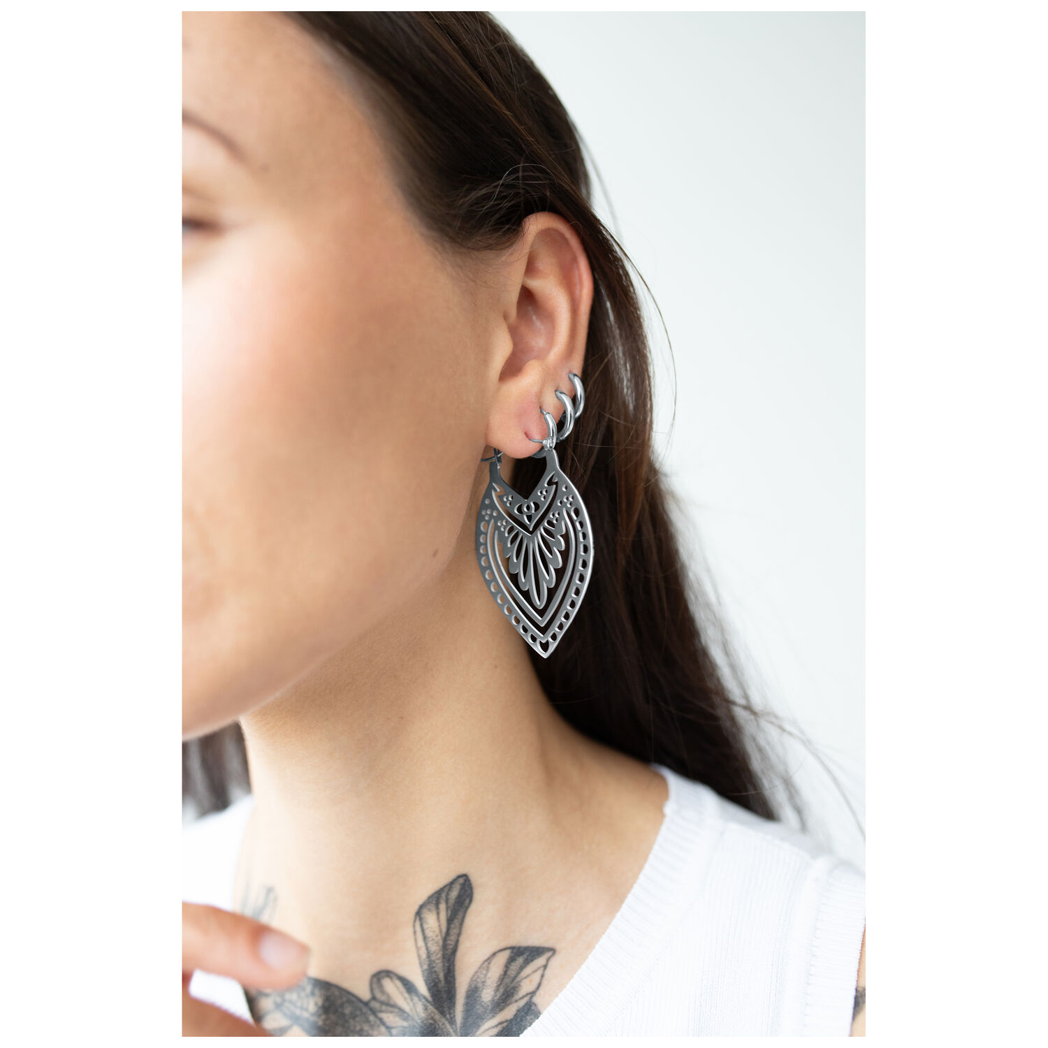 Femme avec des boucles d'oreilles Creek Hoops en argent, portées à l'oreille, fond blanc