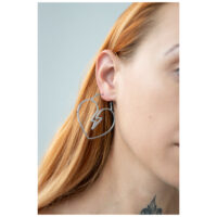 Créoles en forme de cœur en acier chirurgical Créole argentée en forme de cœur avec design éclair à l'oreille d'une femme sur fond gris