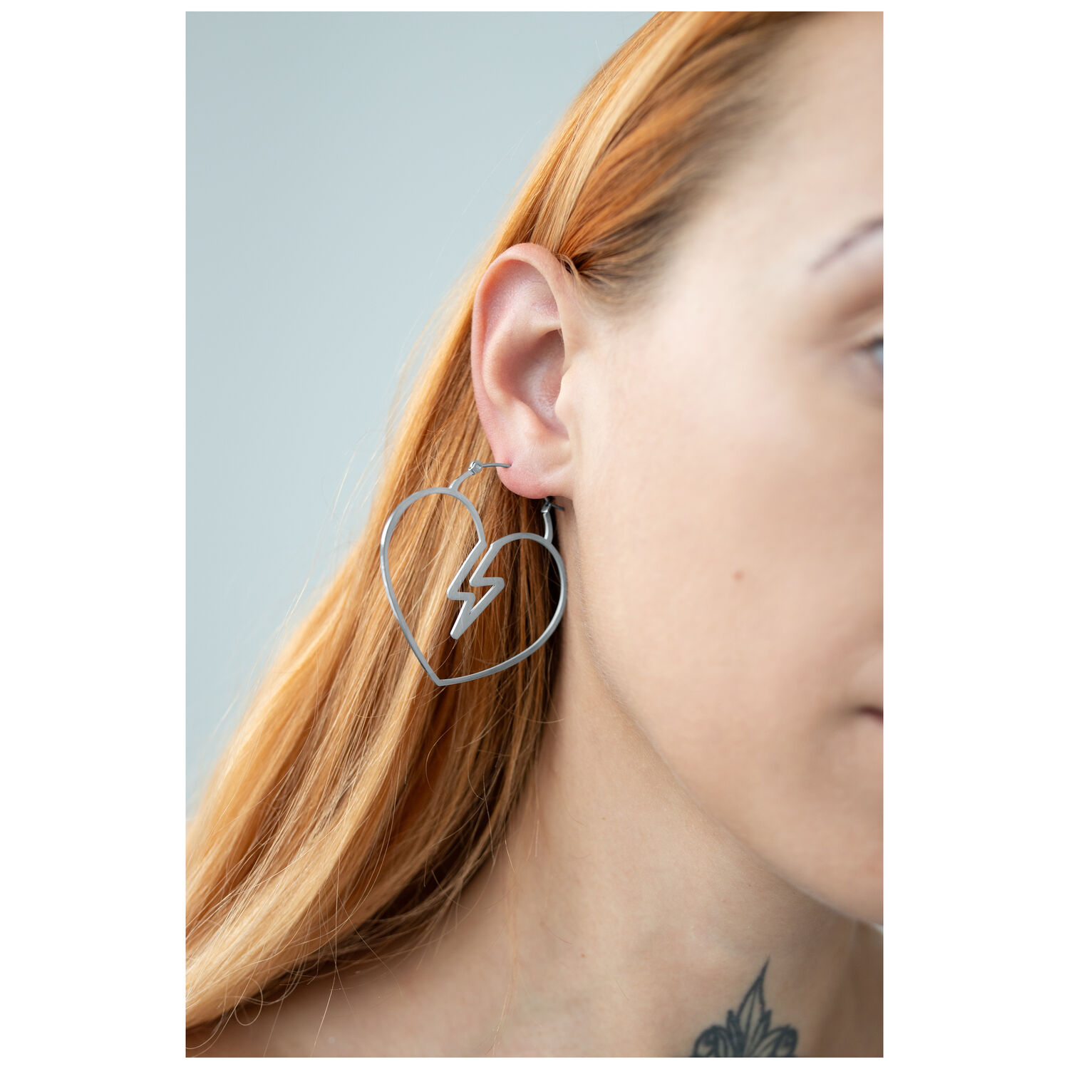 Créoles en forme de cœur en acier chirurgical Créole argentée en forme de cœur avec design éclair à l'oreille d'une femme sur fond gris