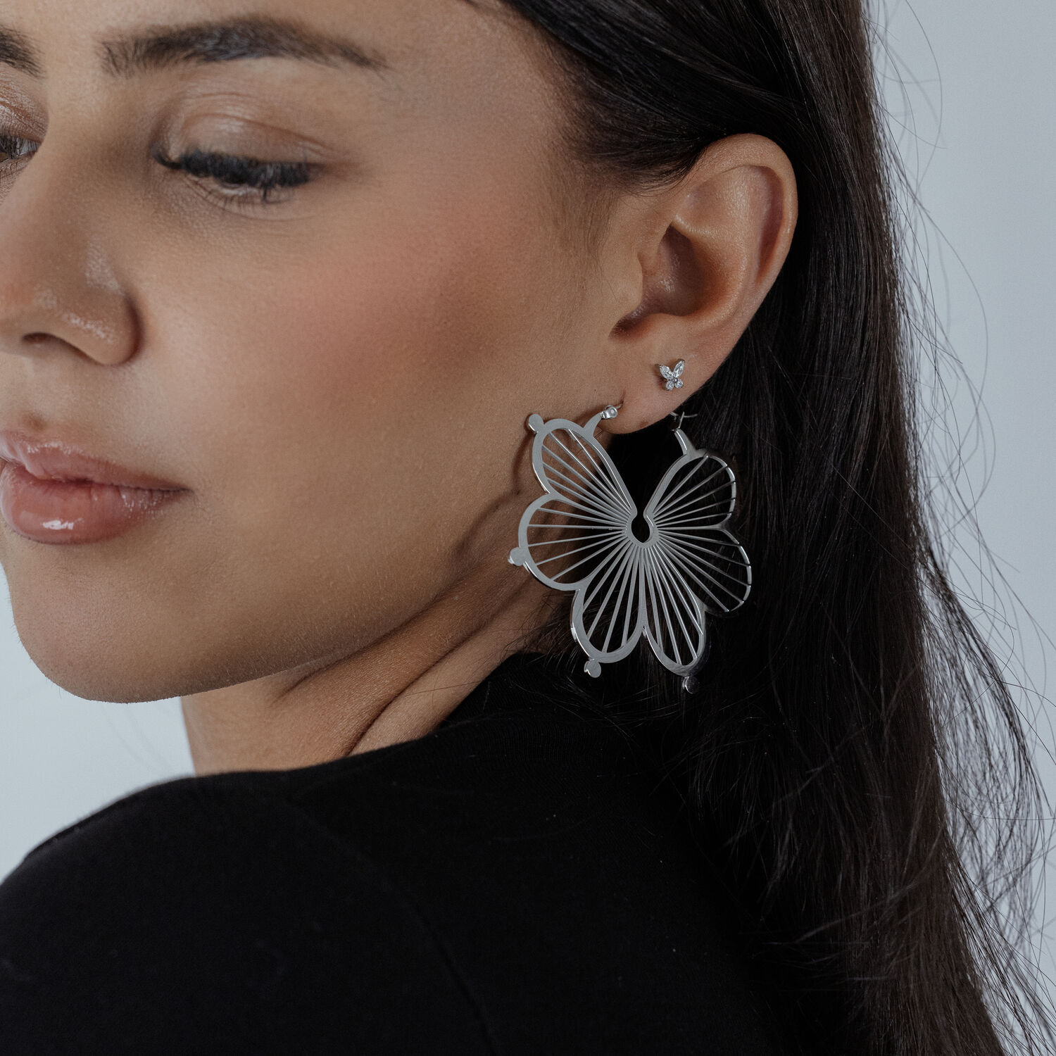 Boucles d'oreilles fleurs en argent à l'oreille d'une femme Boucles d'oreilles fleurs en argent à l'oreille d'une femme avec haut noir, gros plan