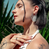 Créoles Noble Leaf en argent et noir Femme avec de grandes boucles d'oreilles en argent devant une plante verte