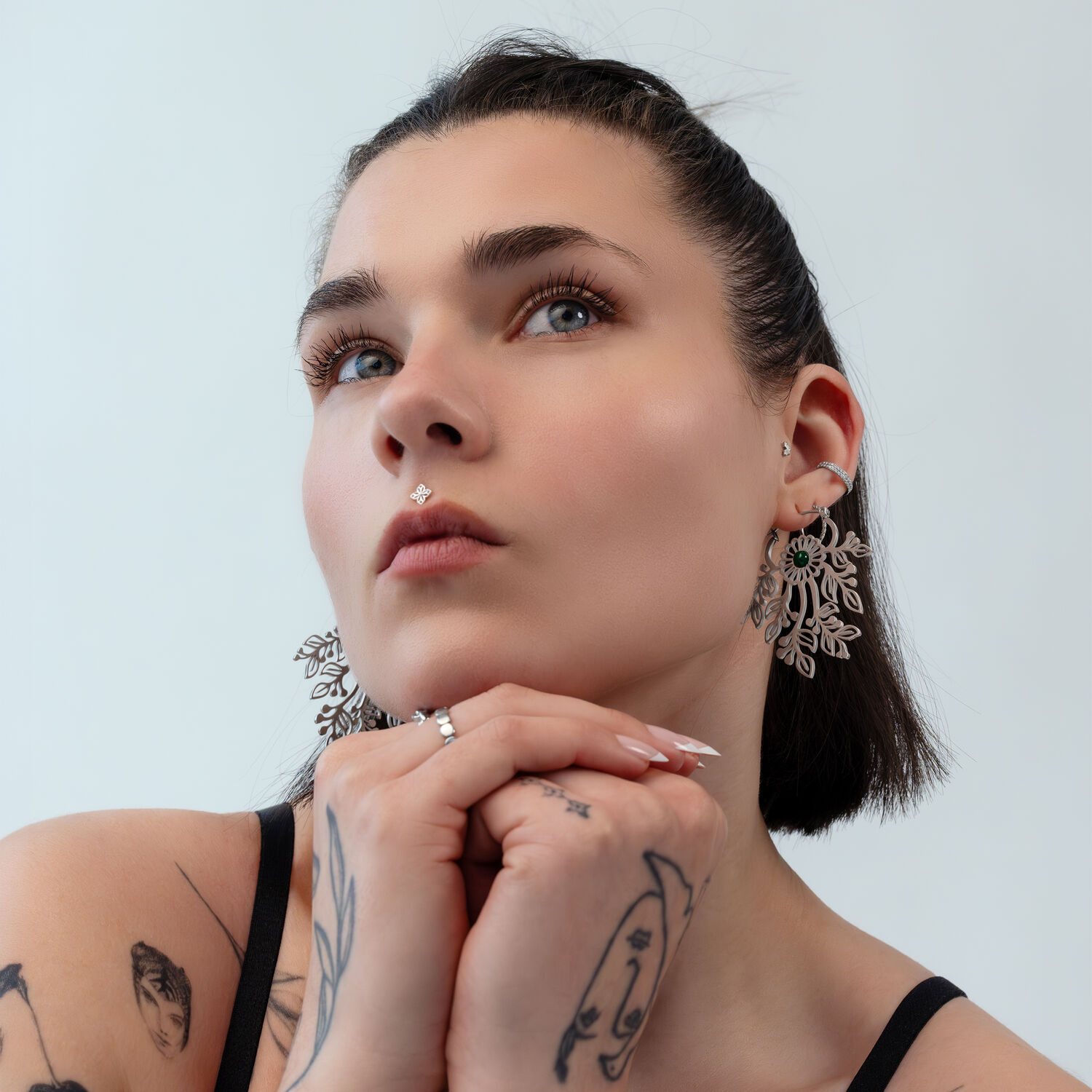 Femme aux cheveux courts portant de grandes boucles d'oreilles délicates en métal argenté sur fond clair