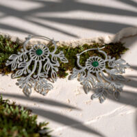 Deux boucles d'oreilles argentées avec des ornements délicats et des pierres vertes sur une surface blanche avec de la mousse