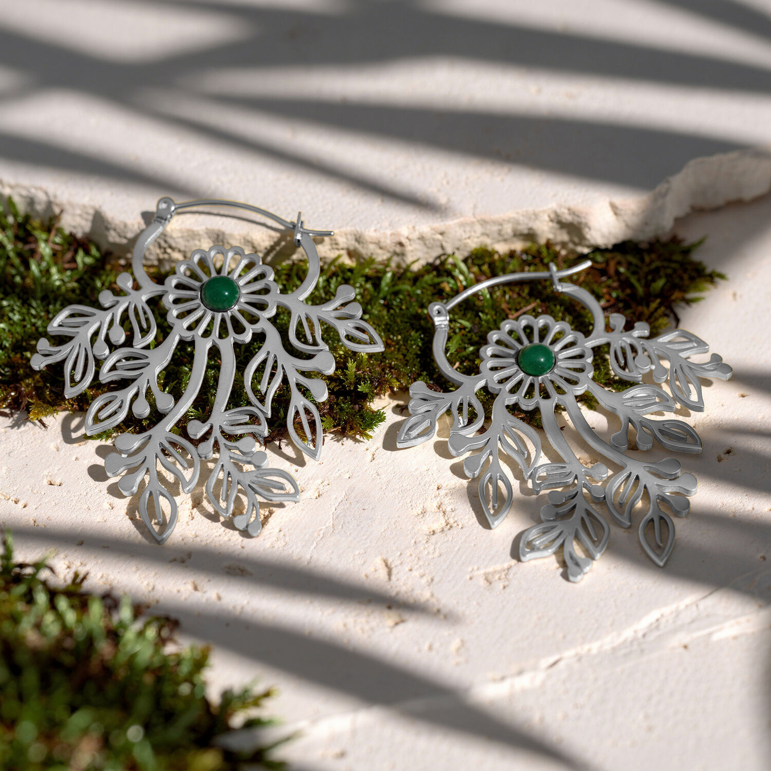 Deux boucles d'oreilles argentées avec des ornements délicats et des pierres vertes sur une surface blanche avec de la mousse
