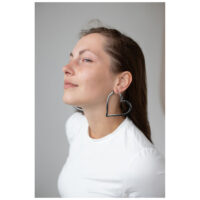 Boucles d'oreilles Heart Hoops stylées en noir Femme portant de grandes boucles d'oreilles noires en forme de cœur sur fond gris