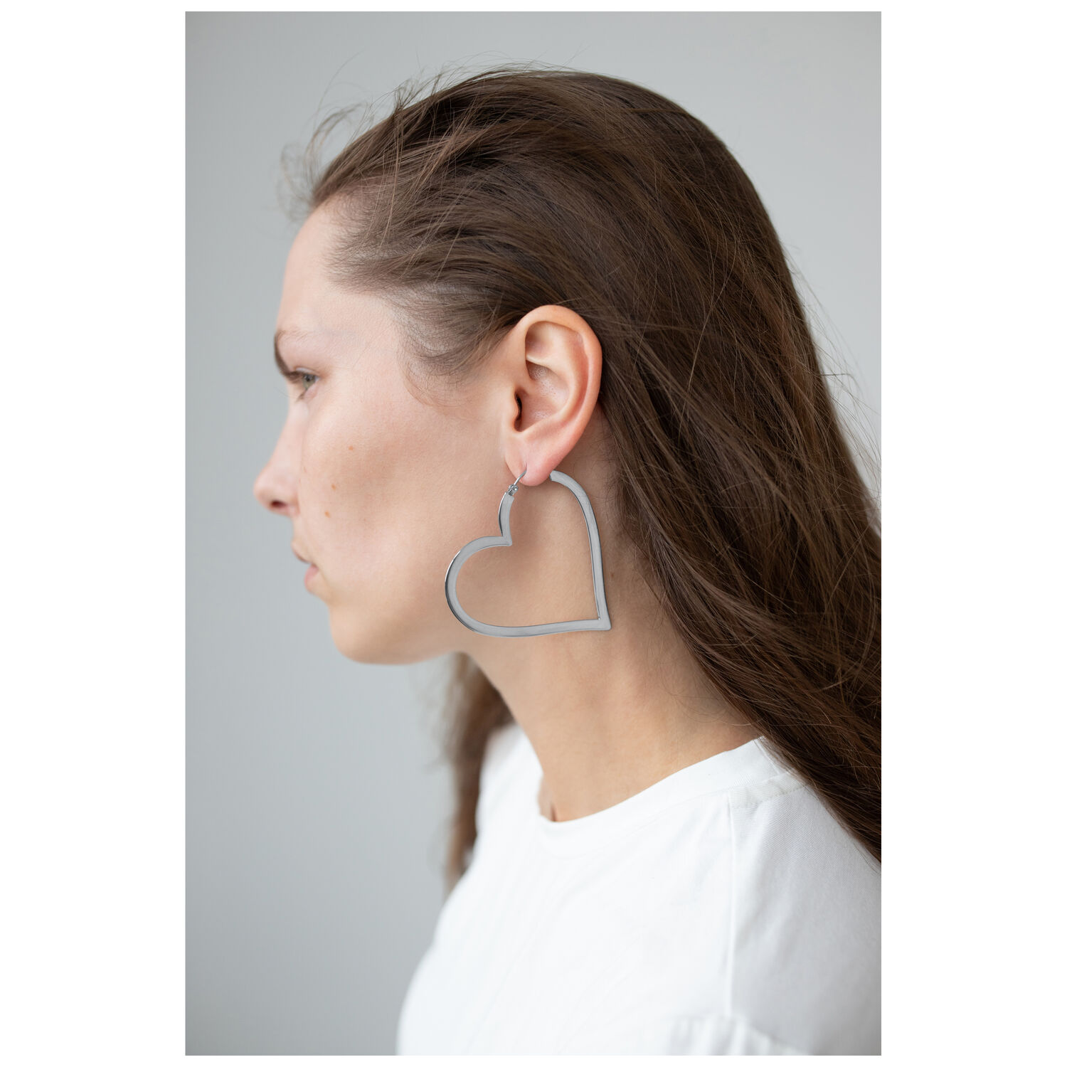 Boucles d'oreilles en forme de cœur en acier inoxydable Femme portant des boucles d'oreilles argentées en forme de cœur, profil latéral