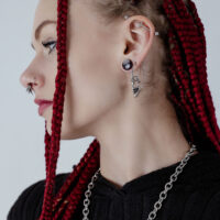 Boucle d'oreille crâne argentée en acier chirurgical Boucle d'oreille crâne argentée en acier chirurgical sur l'oreille d'une personne avec des tresses rouges