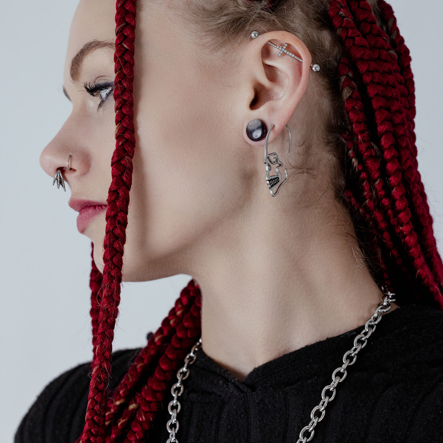 Boucle d'oreille crâne argentée en acier chirurgical Boucle d'oreille crâne argentée en acier chirurgical sur l'oreille d'une personne avec des tresses rouges
