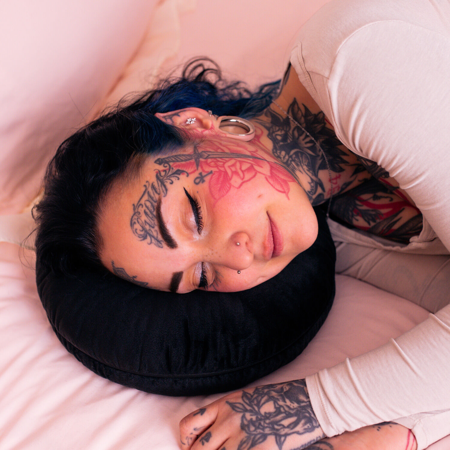 Coussin de perçage Wildcat noir Personne tatouée allongée sur un coussin de perçage noir sur une literie rose