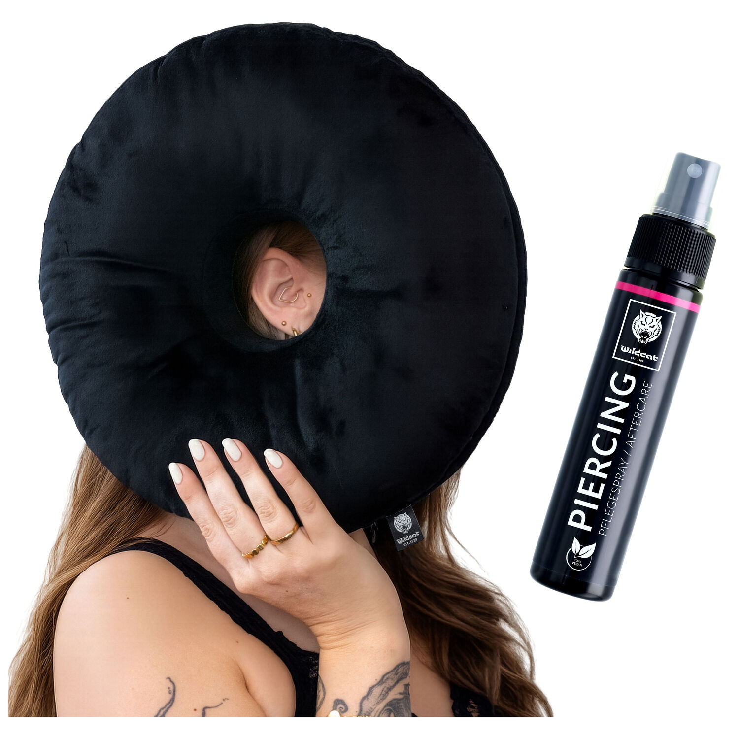 Ensemble de coussin et spray pour piercing Wildcat Coussin noir pour piercing avec trou, tenu par une personne, à côté un spray pour piercing
