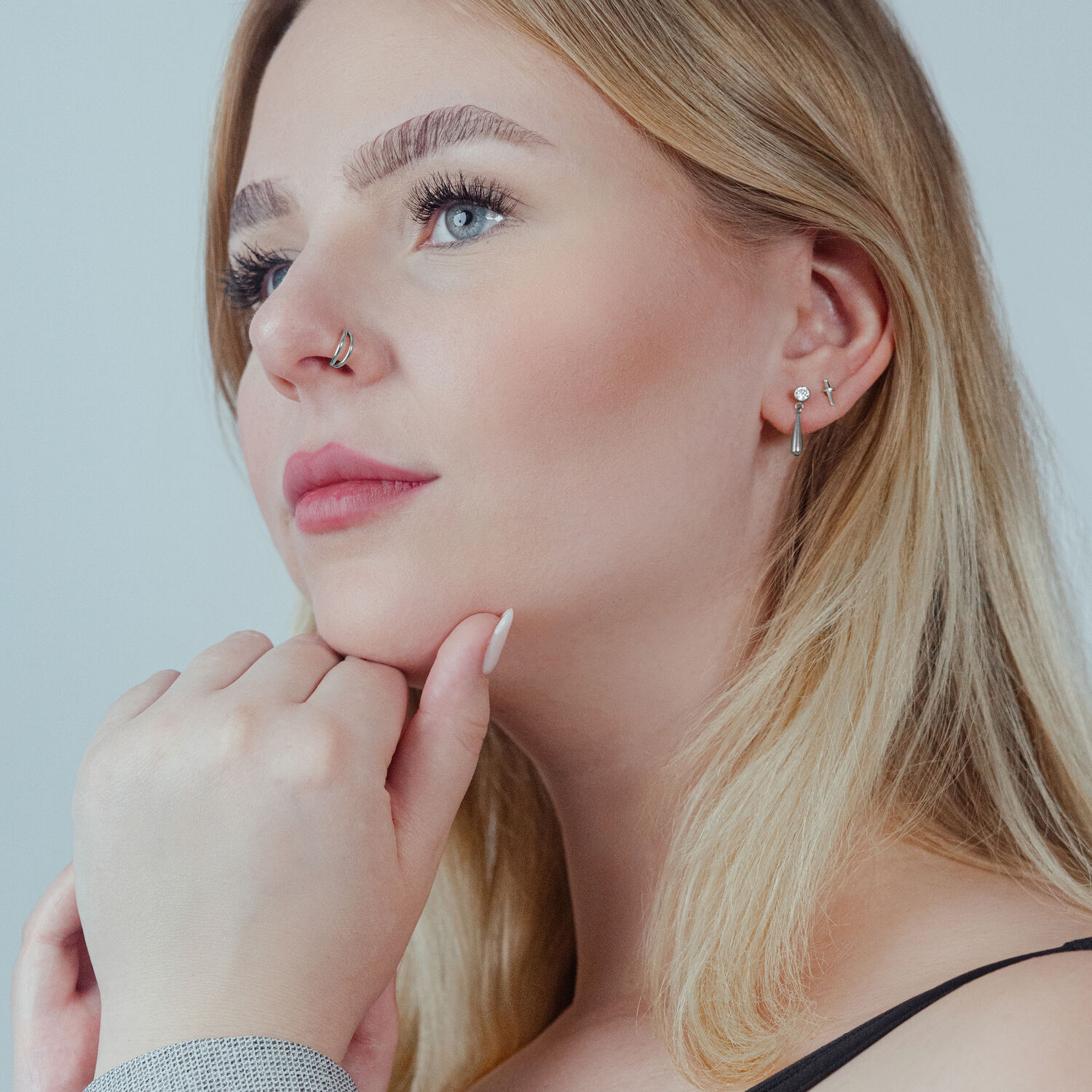 Clicker à double rangée en argent pour oreille et nez Femme portant un clicker à double rangée en argent à l'oreille et un anneau de nez, fond neutre