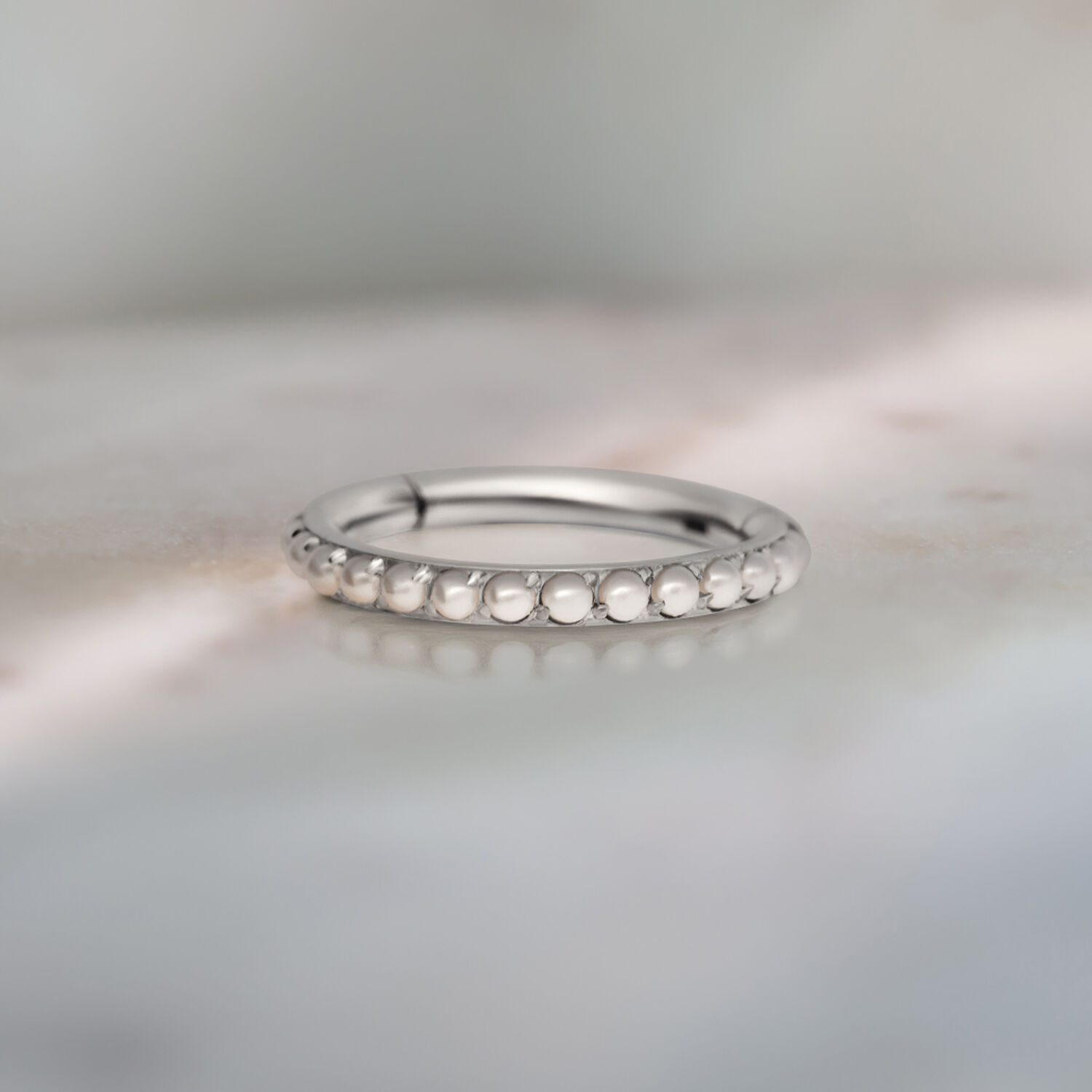 Anneau de piercing argenté avec décoration de perles sur fond gris