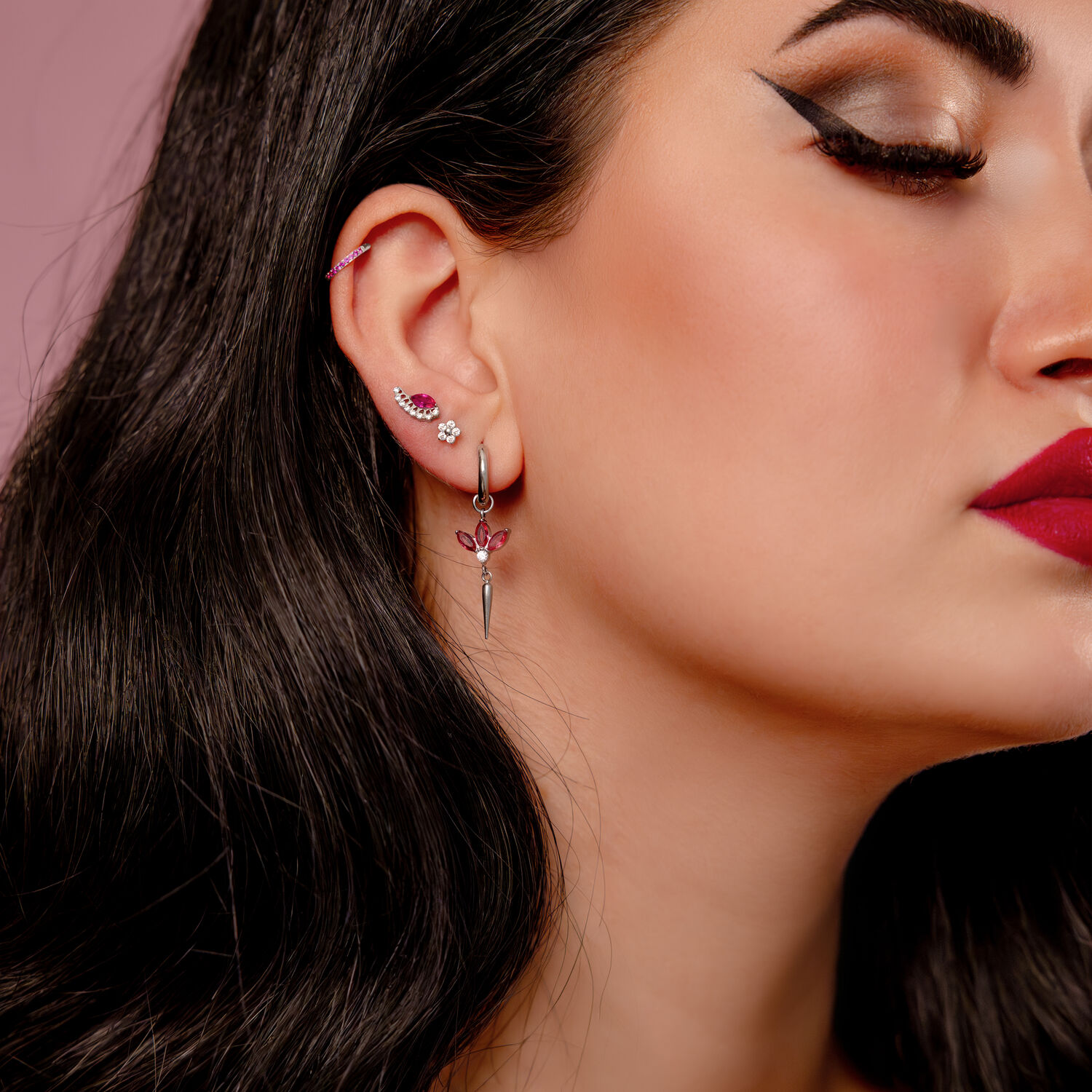 Clicker rubis en argent, 12 mm Gros plan d'une oreille avec plusieurs piercings, dont un clicker argenté avec des cristaux rouges, sur fond rose.