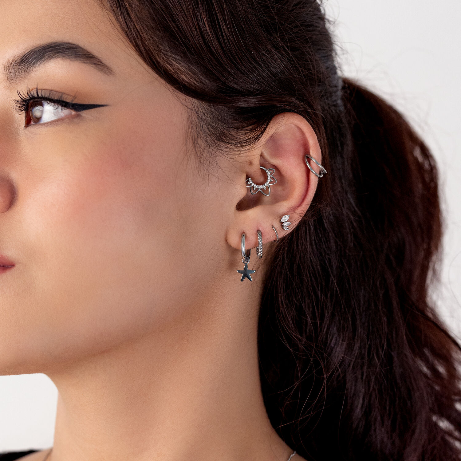 Gros plan d'une oreille avec plusieurs piercings en argent, y compris un pendentif étoile, sur fond blanc